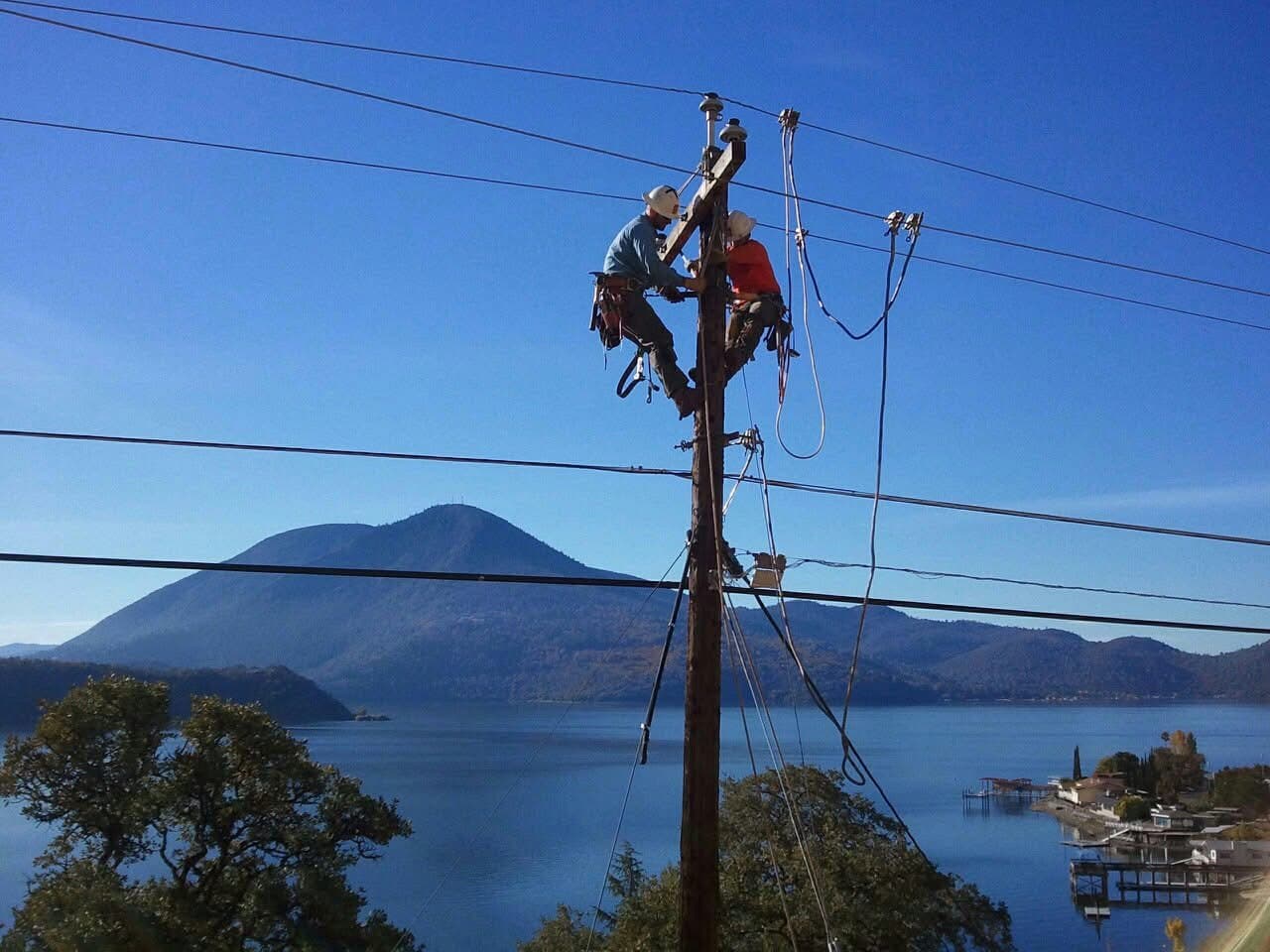 Two IBEW linemen working atop a distribution pole above a lake